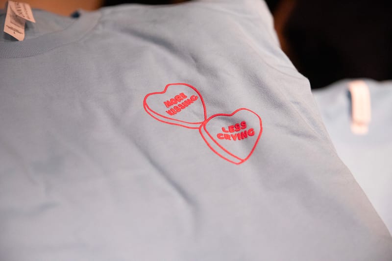 light blue shirt with heart design that says "more kissing less crying"